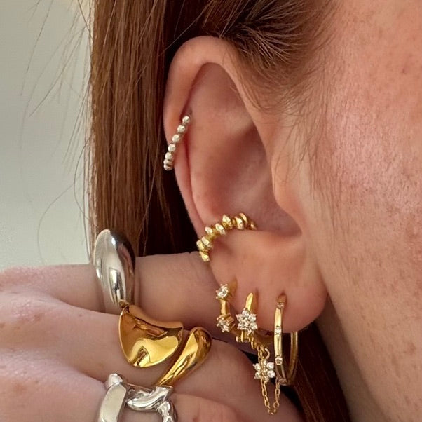 Composition de bijoux hypoallergeniques en argent 925 plaqué or 18k ou rhodié de Luxlab Collection. Mono-boucle IRIS Gold plaquée or portée, deux fleurs scintillantes élevant le style avec subtilité.Boucles d'oreilles LOLA, earcuff GLOSSY, Bagues ALLURE Silver , FLOW gold, Claudy Silver  de Luxlab Collection
