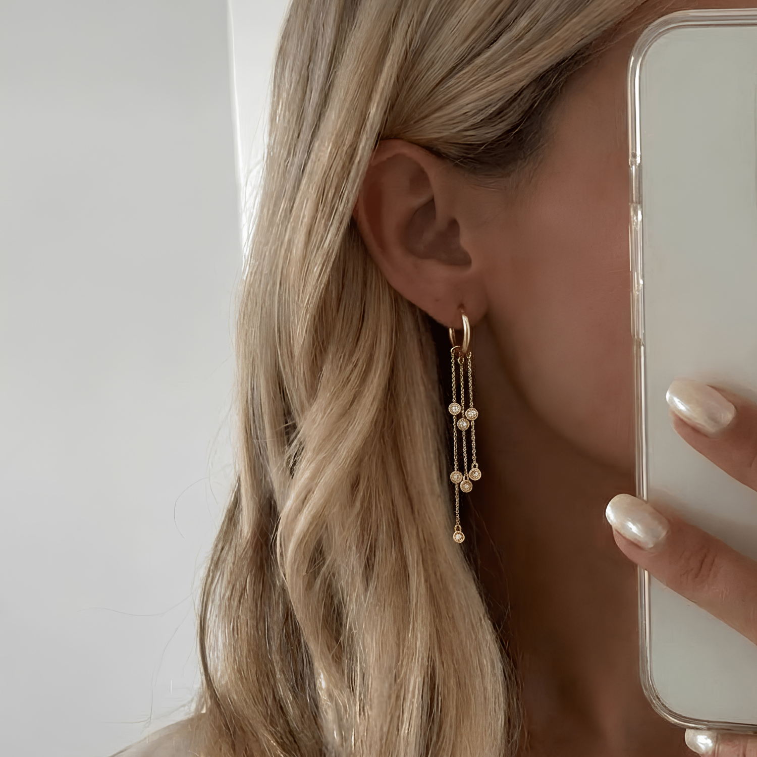 Mono boucle Golden Hour — créole chaînes asymétriques zircons bezel en argent 925 plaqué or 18k. 55mm, hypoallergénique, résistante à l'eau. Effet signature. vue portée par une femme blonde en selfie